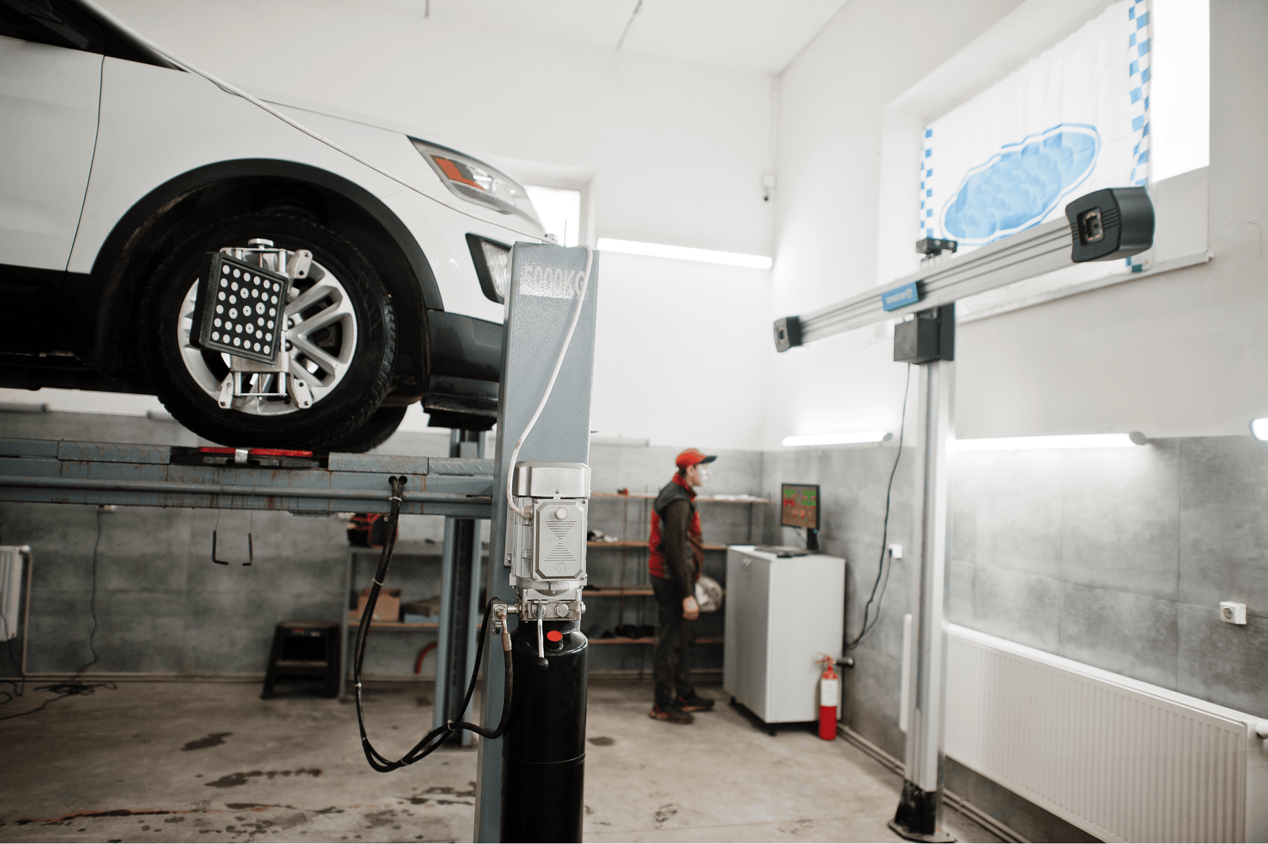 White SUV on lift undergoing computerized wheel alignment in service garage