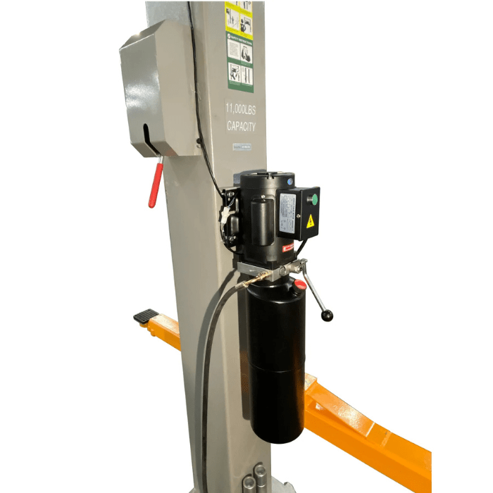 Close-up of the Triumph NTO-11A 11,000 lb Two-Post Overhead Car Lift’s hydraulic motor and pump assembly attached to the gray column, with bright orange arms visible in the background.