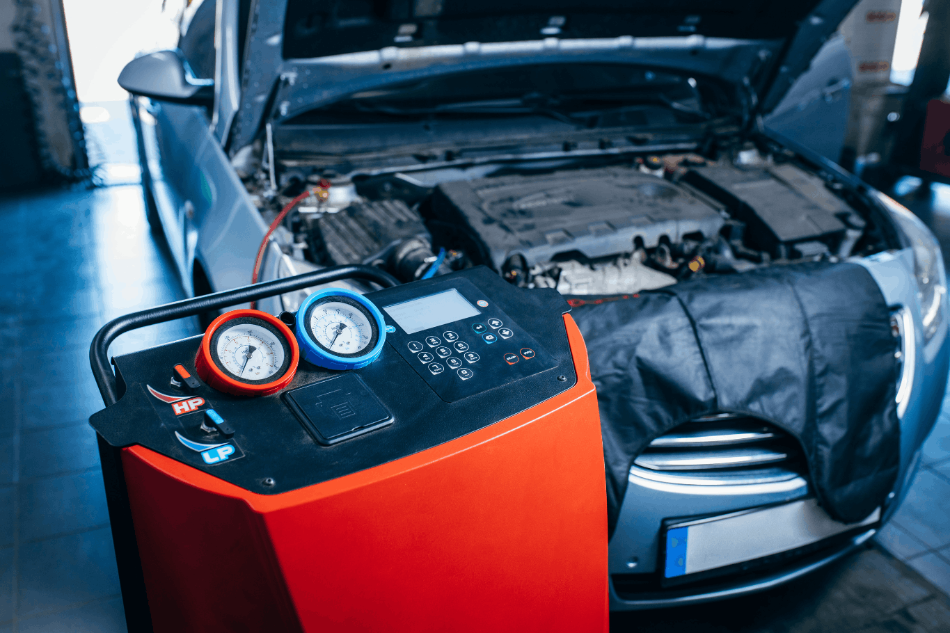 Automotive air conditioning service machine connected to a car with its hood open in a repair shop.