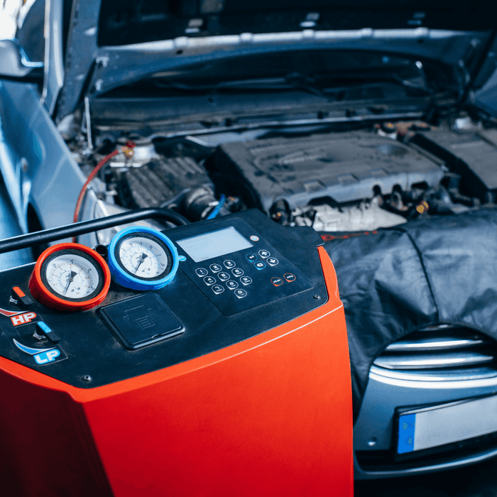 Automotive air conditioning service machine connected to a car with its hood open in a repair shop.