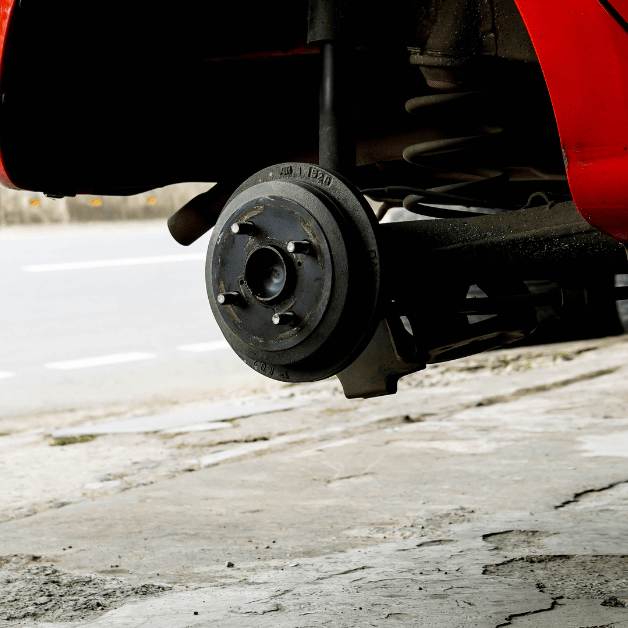 Car on jack stands with wheel removed, drum brake and suspension visible on driveway.