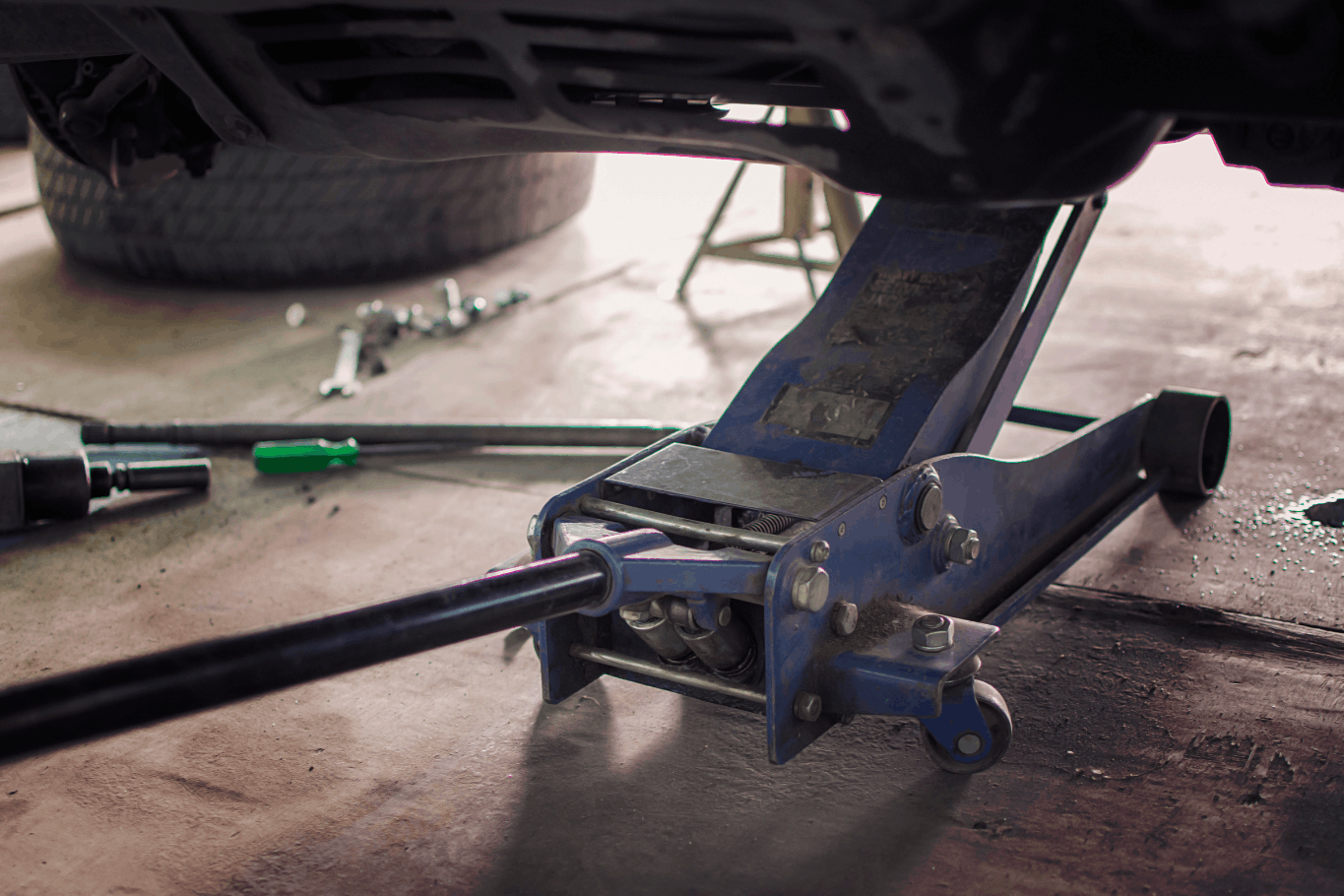 Hydraulic floor jack lifting a vehicle in an automotive repair garage.