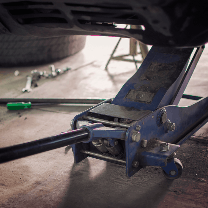 Hydraulic floor jack lifting a vehicle in an automotive repair garage.