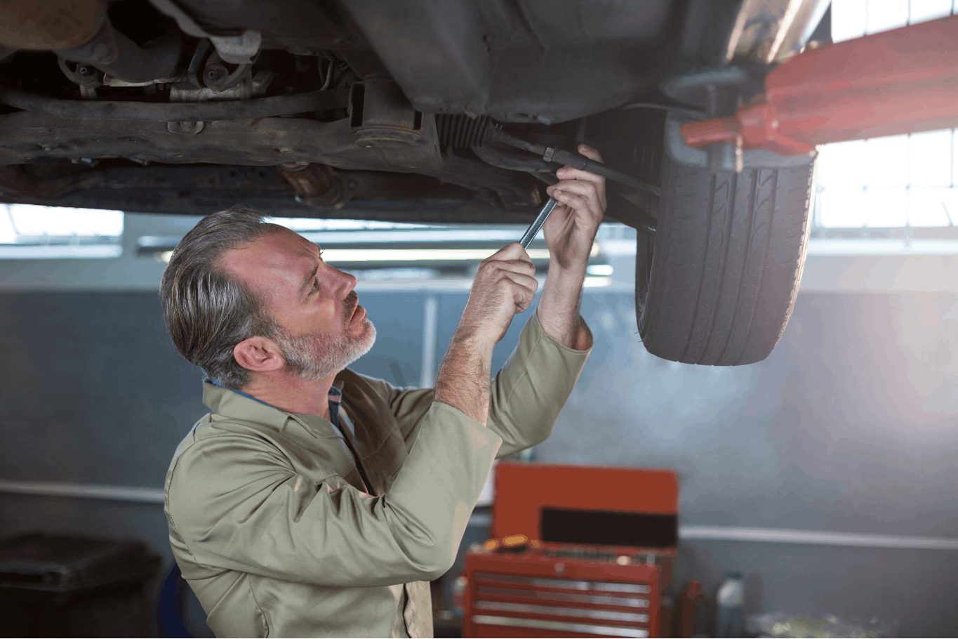 Technician working under a lifted car during suspension and steering inspection