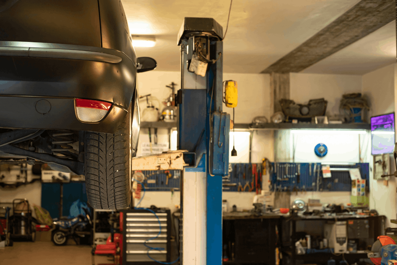 Vehicle raised on a two-post lift inside an automotive repair shop with tools and equipment in the background.