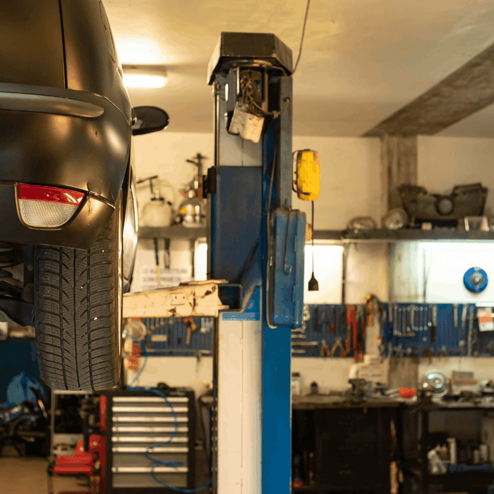Vehicle raised on a two-post lift inside an automotive repair shop with tools and equipment in the background.