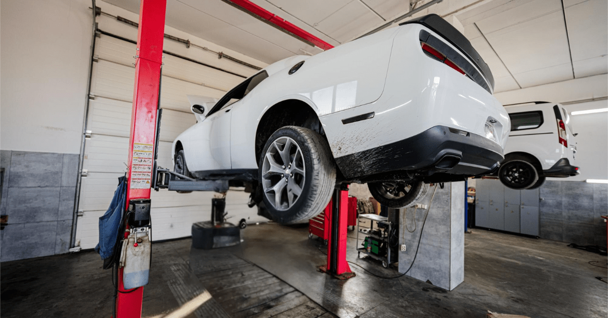 White Dodge Challenger lifted on a red 2-post car lift inside an auto repair shop.