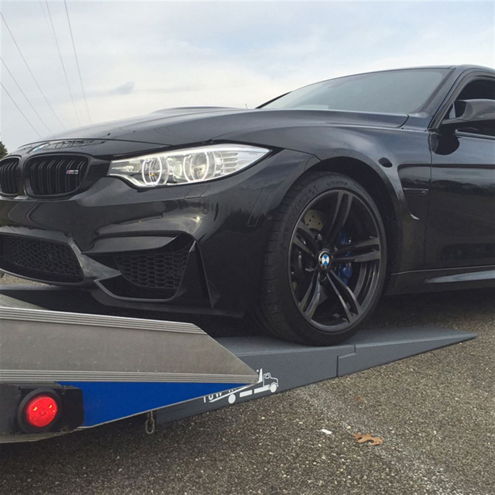 Black BMW M3 loading onto a rollback flatbed over Race Ramps tow ramps