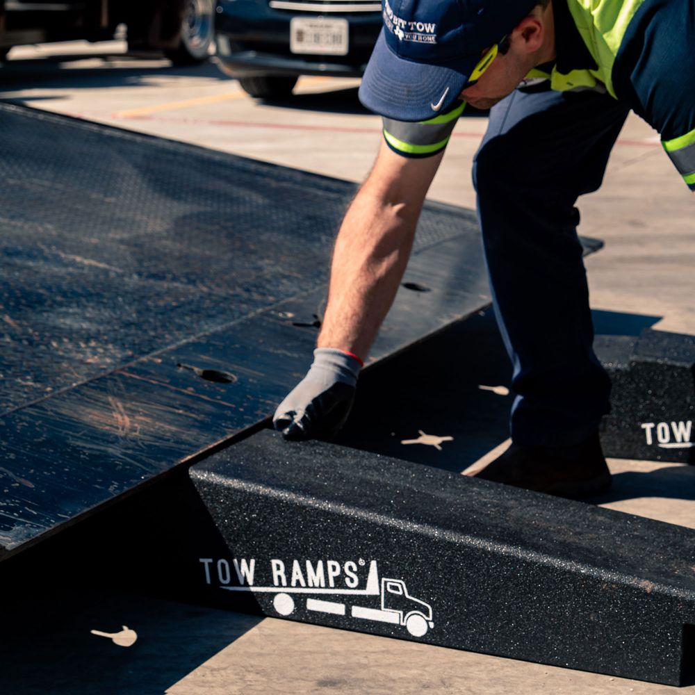 Tow operator setting a Race Ramps tow ramp against the deck of a rollback carrier