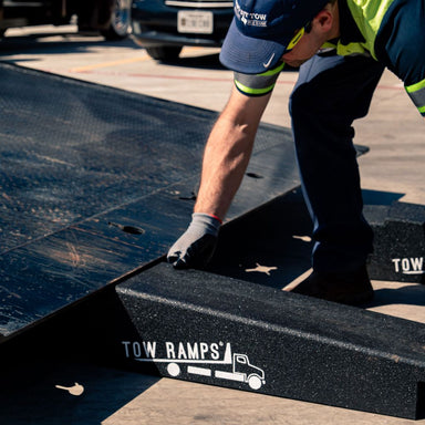 Tow operator setting a Race Ramps tow ramp against the deck of a rollback carrier