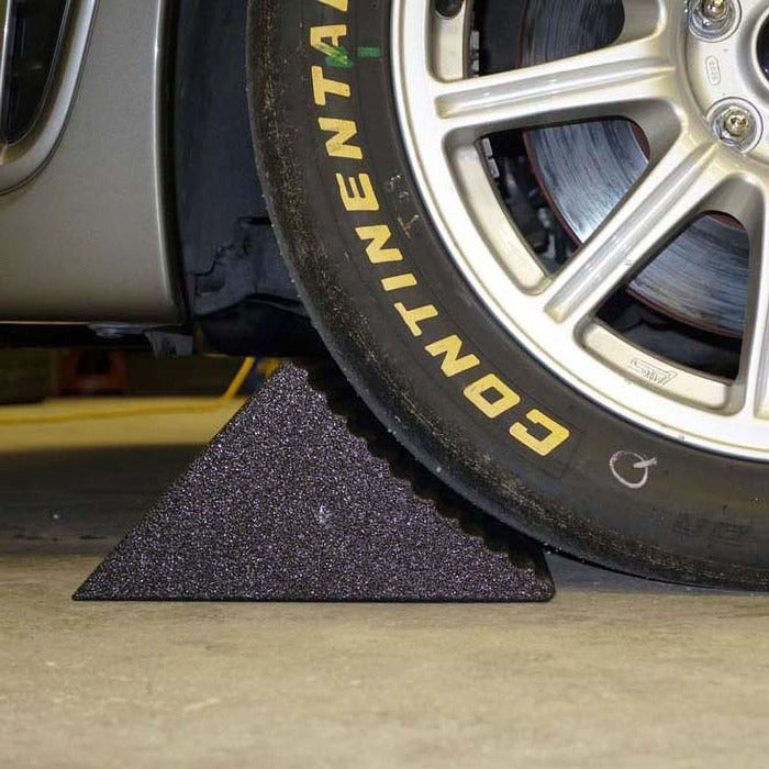 Race Ramps Racer Chock wedged against a car tire on concrete