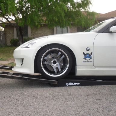 White sports car with a front splitter climbing a Race Ramps RR-TR-6 trailer ramp